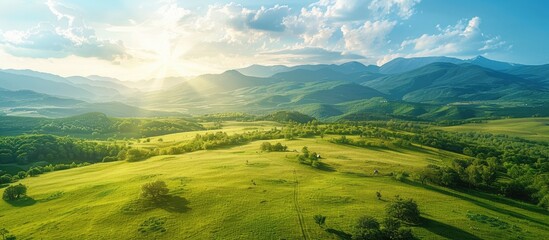Poster - Aerial view landscape showing a green meadow in the countryside during spring or summer with a sunny day backdrop of mountains perfect for copy space image