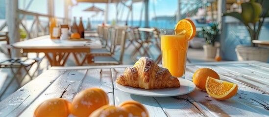 Poster - A European style breakfast with a croissant a glass of juice and fresh oranges on a white wooden table at a marina restaurant offering a copy space image for food and drink items
