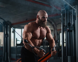 Wall Mural - Bald Caucasian bodybuilder training chest using cable crossover in gym. 