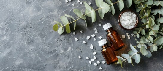 Poster - A flat lay display features aromatherapy products like essential oil bottles sea salt and eucalyptus branch on a grey background offering copy space image