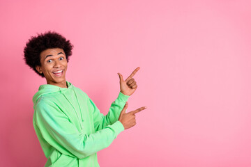 Wall Mural - Portrait of nice young man indicate fingers empty space wear green hoodie isolared on pink color background