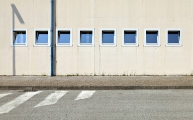 Wall Mural - Cream color plaster wall with row of small insulated windows in an industrial building. Sidewalk and road in front. Background for copy space.