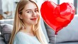 © suyu - Blonde Beautiful Girl Sitting on Couch with Red Heart-Shaped Balloon, Celebrating Valentine's Day with Joyful Expression, Perfect for Valentine's Day Themes and Romantic Concepts