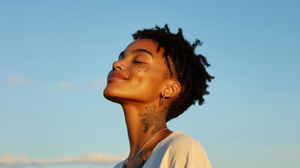 Wall Mural - Smiling woman with short curly hair and tattoos, enjoying moment under clear blue sky. Her expression radiates joy and tranquility. 