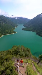 Wall Mural - Plansee Austria, An absolutely captivating landscape that showcases a tranquil lake beautifully surrounded by majestic mountains. A couple of man and woman hiking in the mountain alps of Austria 