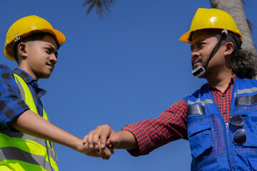 two Asian construction workers shake hands during construction site survey, cooperation agreement, construction work concept.