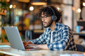 Wall Mural - Focused young adult male entrepreneur with curly hair using laptop and headset in a modern office setting, embodying professionalism and dedication, Generative AI