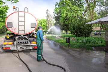 A man in a green jumpsuit is spraying water from a truck onto the road