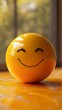 © Kakabe - A bright yellow smiley face ball with a joyful expression sits on a warm, sunlit surface, creating a cheerful and positive atmosphere ideal for use in marketing, mental health awareness