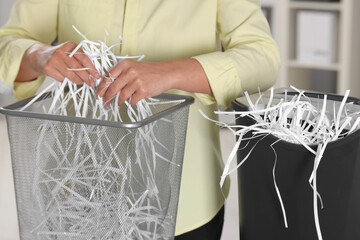 Wall Mural - Woman putting shredded paper strips into trash bin indoors, closeup