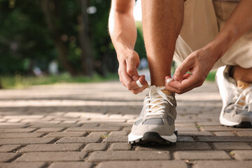 Wall Mural - Man tying shoelace of grey sneaker outdoors, closeup. Space for text