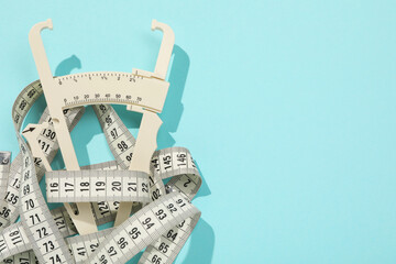 Poster - Plastic body fat caliper and measuring tape on light blue background, top view. Space for text