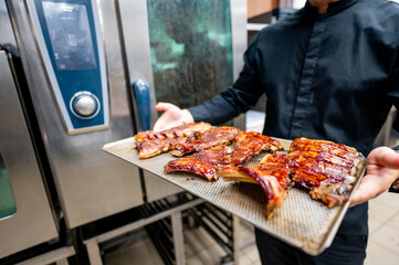 Canvas Print - A chef in a professional kitchen presents a tray of glazed ribs, showcasing the delicious and visually appealing dish. Ideal for culinary, restaurant, or food-related content.