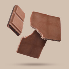 Wall Mural - Pieces of sweet chocolate falling on beige background