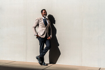 Wall Mural - Mature black businessman wearing elegant suit strolling in the city - Corporate african adult senior male with gray beard