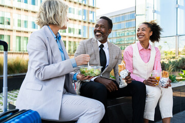 Group of multiethnic business people meeting outdoors during lunch pause from work - International corporate business team bonding in the city and eating take-away salad and sanwiches