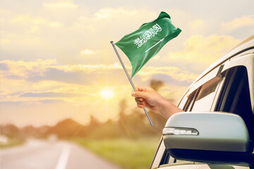 Waving the Saudi Arabia flag against the sunrise or sunset from a car driving along a country road. Holding the Saudi Arabia flag, traveling by car, on a weekend trip.