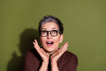 Sticker - Photo of gray hair beautiful cheerful pensioner grandmother in brown t shirt and eyeglasses looking crazy up isolated on khaki color background