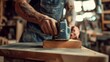 © Pascal - Detailed image showing craftsman using electric sander on wooden piece in workshop. Forearm with tattoo visible, emphasizing intricate work on smoothening wood surface