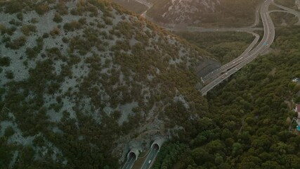 Wall Mural - aerial view of highway in the mountains between dense forest at sunset. Tunnel in the mountains. Movement