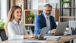 © ZinaZaval - A man and woman engage in a work meeting, focusing on their laptops in a modern office filled with greenery and natural light