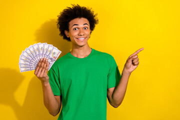 Poster - Photo of funky cool guy dressed green t-shirt holding money fan pointing emtpy space isolated yellow color background