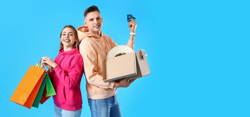 Canvas Print - Young couple with credit cards, shopping bags and parcel on blue background with space for text