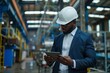 © Oleksandr - Focused African American engineer in suit and hard hat working on tablet in factory.