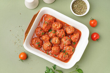 Wall Mural - Baking dish of tasty meat balls with tomato sauce and parsley on green background