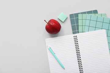 Notebooks with fresh red apple and stationery on grey background