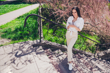 Poster - Full length photo of pretty young good mood girl stand stairs hold device wear white clothes walk outside urban city park