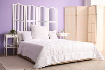 Sticker - Interior of stylish bedroom with comfortable bed, white pillows, bedside tables and folding screen