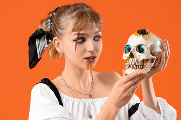 Poster - Young woman dressed for Halloween with skull and jelly candies on orange background, closeup