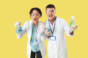 Wall Mural - Shocked young chemists with flasks on yellow background