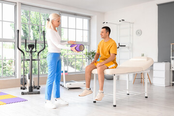 Poster - Female physiotherapist giving foam roller to young man in rehabilitation center