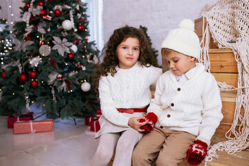 Cute little children near Christmas tree and light on background. Merry Christmas and Happy Holidays.