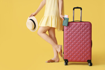 Wall Mural - Young woman with suitcase, hat, passport and ticket on yellow background