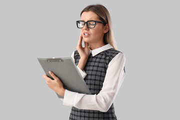 Canvas Print - Young businesswoman with clipboard suffering from tooth ache on grey background