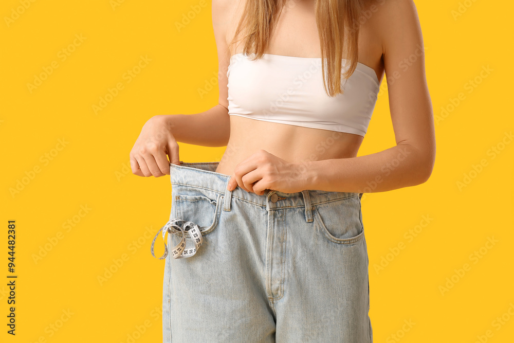 Young woman in loose jeans on yellow background. Weight loss concept