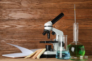 Wall Mural - Modern microscope with chemical flasks, petri dish and book on table against wooden background