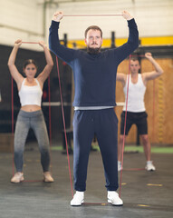 Wall Mural - Strong young man training with rubber band in sports hall during crossfit workout