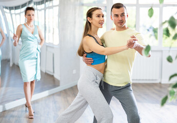 Wall Mural - Guy and girl in sports clothes, under guidance of mentor, practice waltz in choreographic studio. Couple trains waltz performance, takes lessons from choreographer to stage wedding dance