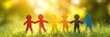 © Helois - Six colorful paper dolls stand in a row holding hands in a field of green grass with a bright sunny bokeh background.