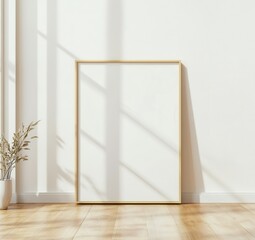 A slim golden picture frame stands against the wall, surrounded by wooden flooring and soft natural light, creating a serene and minimalistic atmosphere. Mockup