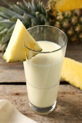 Sticker - Tasty pineapple smoothie in glass and fruit on wooden table, closeup