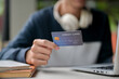 © bongkarn - A close-up image of a man holding a credit card over a table while using his laptop.