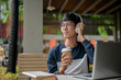 © bongkarn - A positive, thoughtful Asian man gazes at the view while working at an outdoor table.