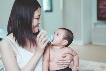 Mother feeding milk to adorable asian baby boy on lap,Newborn child