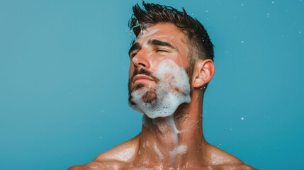 Wall Mural - Closeup portrait of a Caucasian man applying aftershave with a splash across his face in a deep depth of field studio setting with a blue background