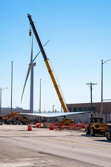 Wall Mural - A crane lifts a wind turbine blade into place with a clear sky behind. Workers guide the blade as other turbines are under construction